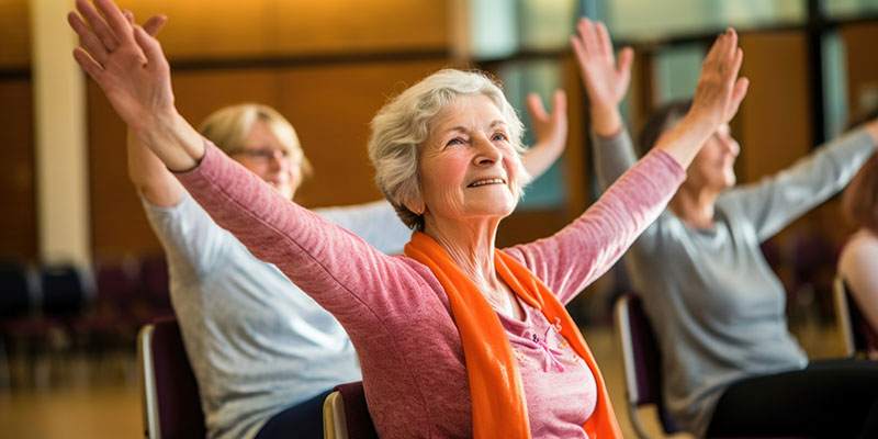 An engaging snapshot showcasing elderly participants comfortably seated on chairs, demonstrating chair yoga exercises that target the wrists and hands, enhancing joint mobility and flexibility